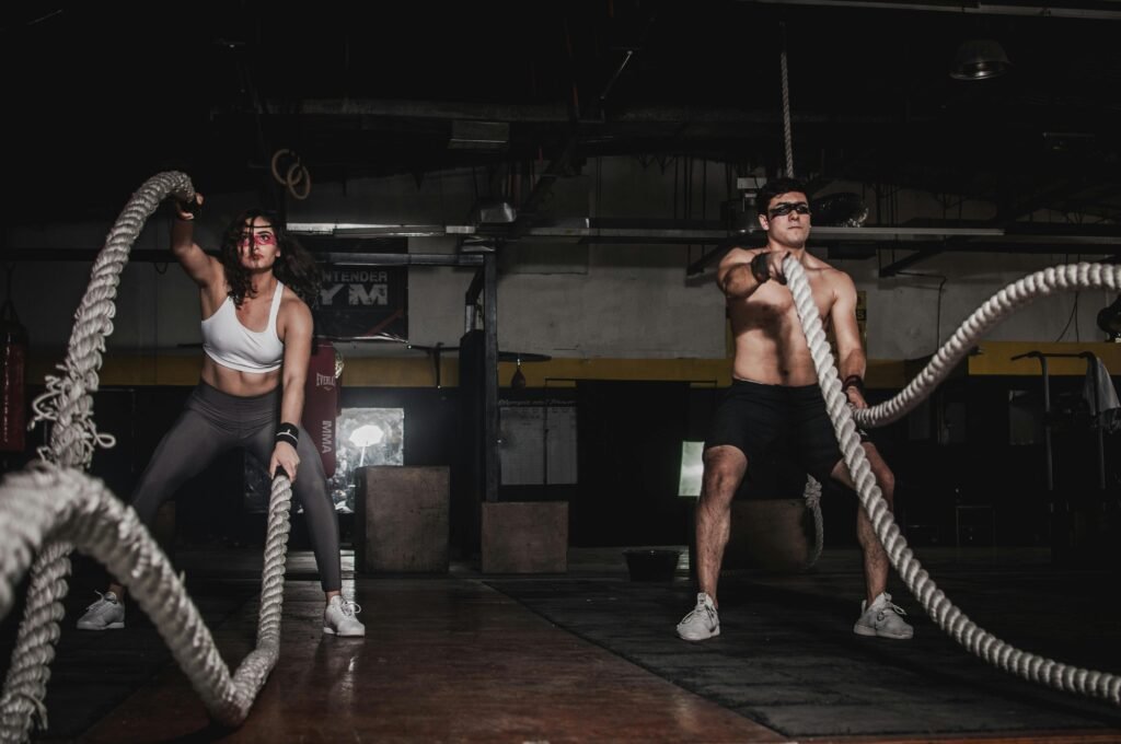 Inicio Two people engage in a powerful indoor battle rope workout, showcasing strength and energy.
